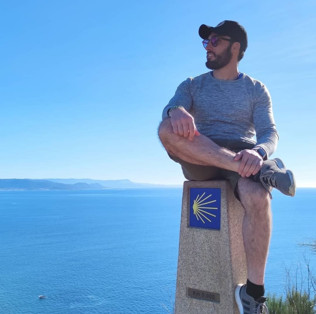 L'immagine rappresenta l'autore, Giovanni Pagoria seduto sulla colonna del km 0 dopo il viaggio di Santiago, con vista sul mare.
